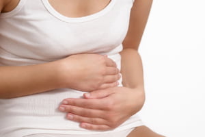 Woman with acute abdominal pain clutching her stomach with her hands as she becomes stressed by the ongoing cramps, torso view of her hands and tummy isolated on white